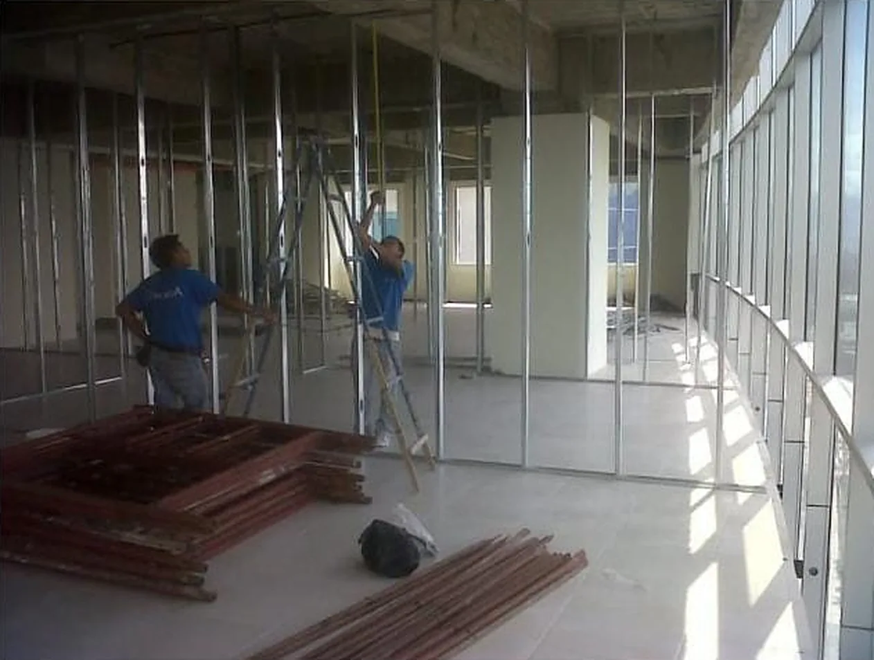 Cuadrilla armando estructura de tablaroca en un espacio amplio con ventanales curvos